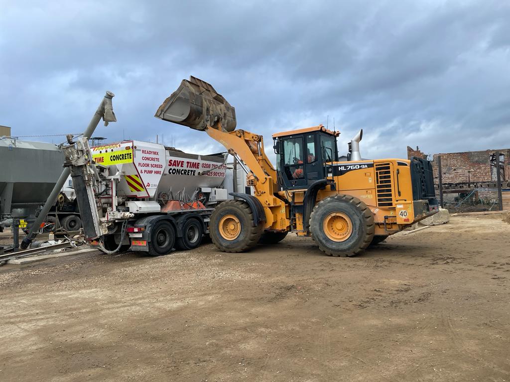 A large front loader transports crushed stone or gravel in a bucket at a construction site